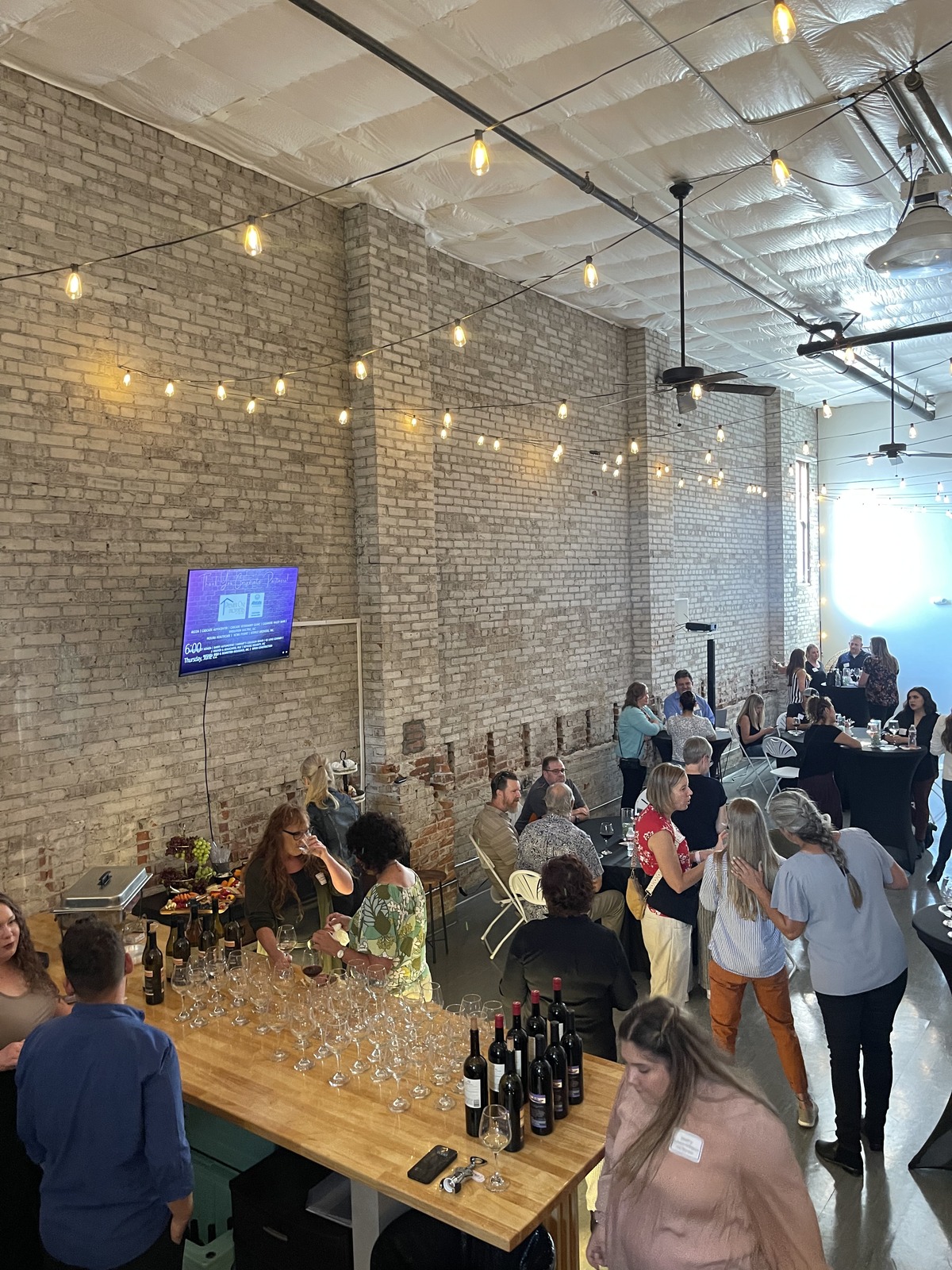 Guests at a wine tasting business mixer under string lights in the brick event space at Host Wenatchee