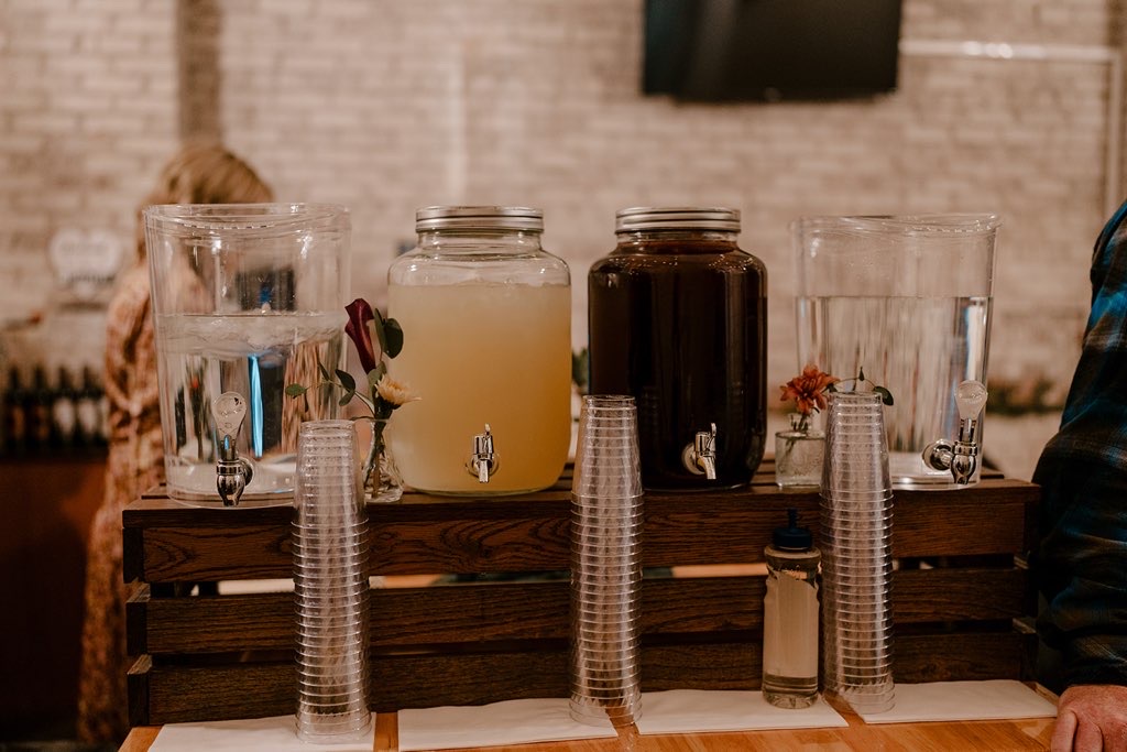 Self-serve drink bar with lemonade, iced tea and water dispensers on a wood crate stand at a Host wedding