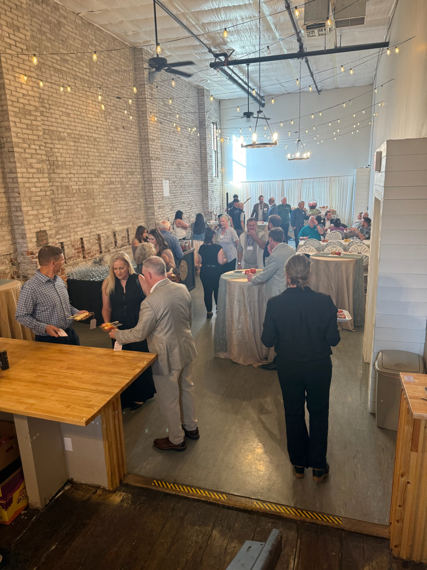 Business guests mingling at cocktail tables under string lights at a corporate mixer in downtown Wenatchee