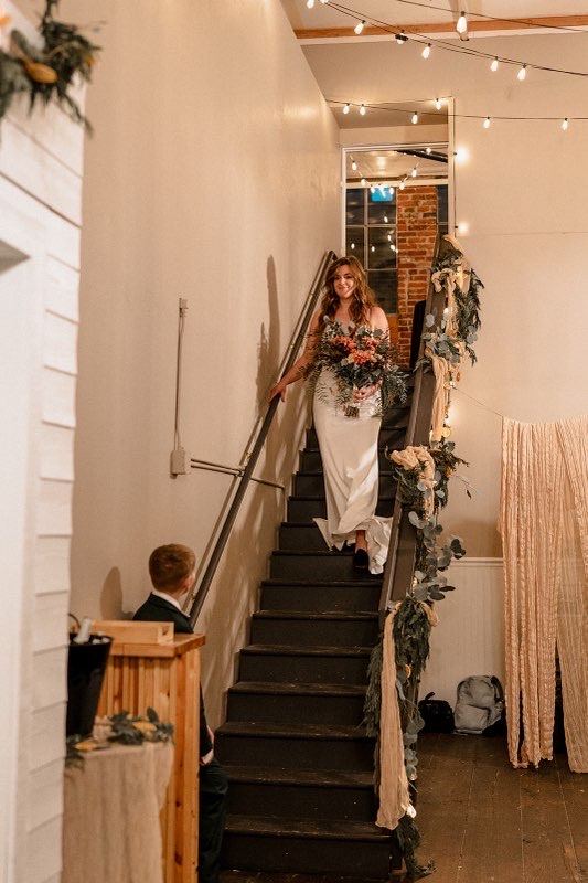 Bride walking down the greenery-draped staircase at Host Wenatchee wedding venue