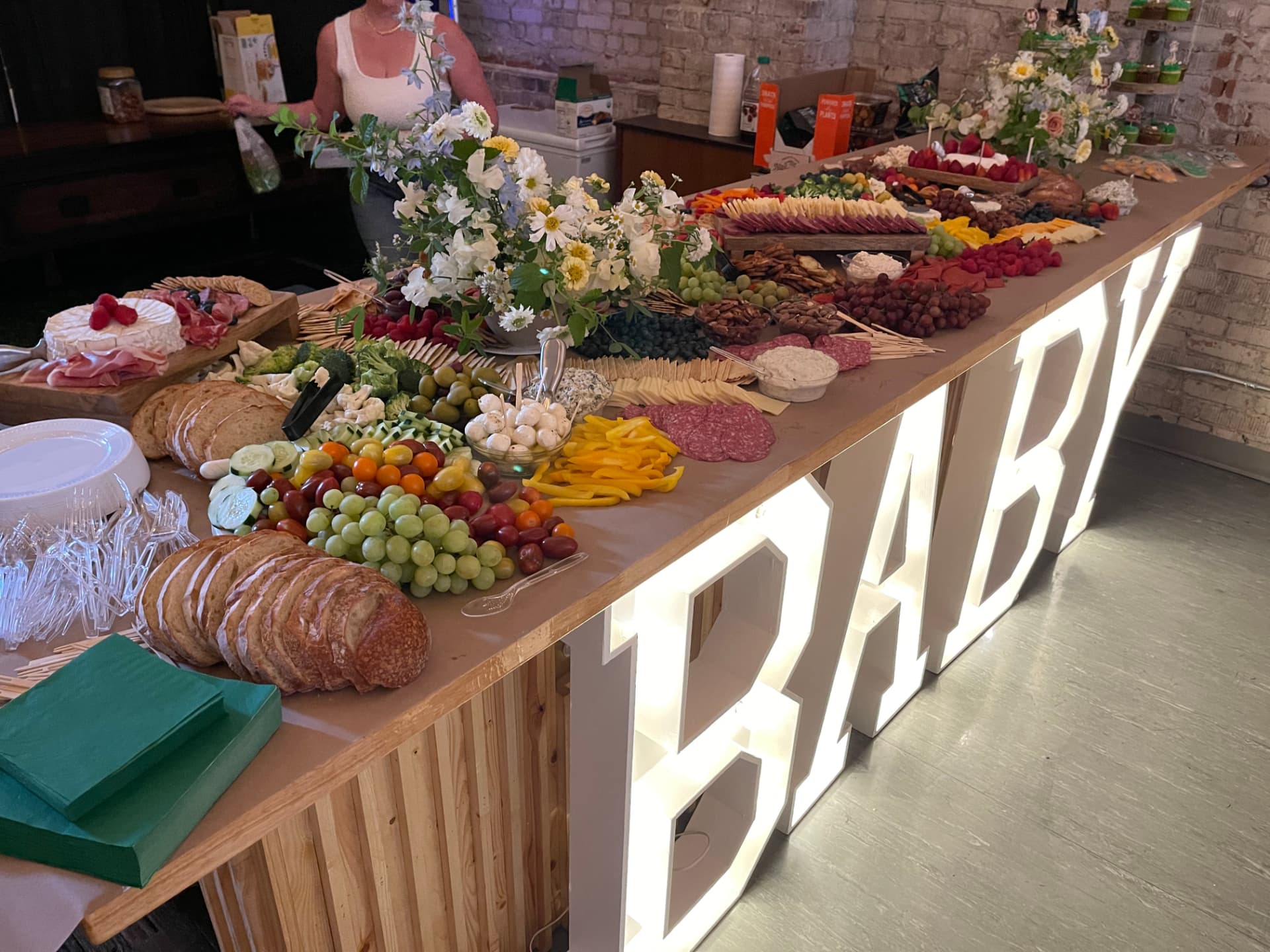 Light-up BABY marquee letters beside a grazing table of charcuterie and fruit