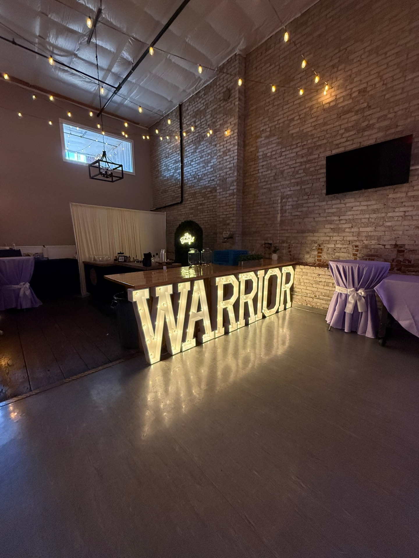 Glowing WARRIOR marquee letters in front of the wood bar at a themed celebration at Host Wenatchee