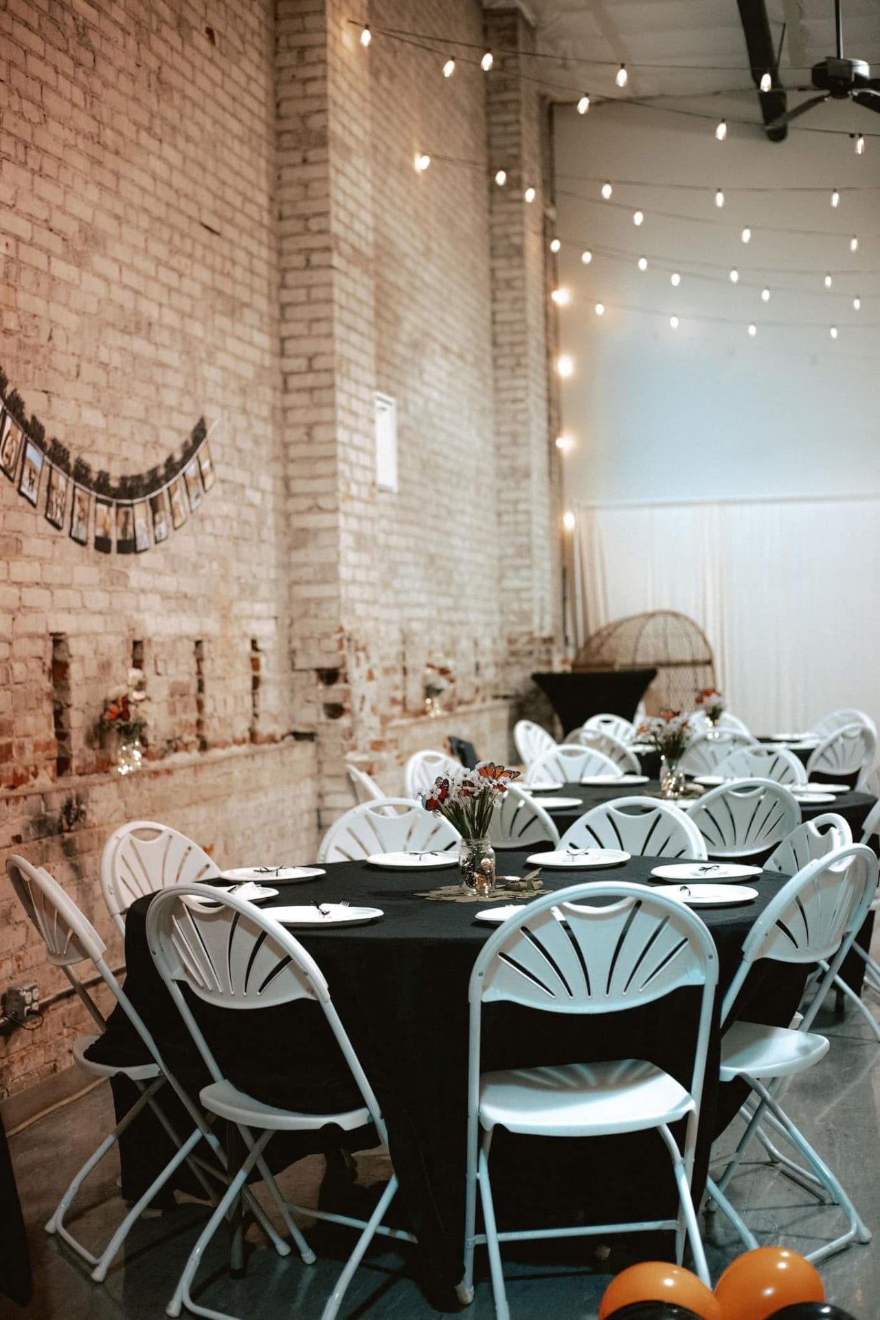 Round tables with black linens and white chairs in the brick event space