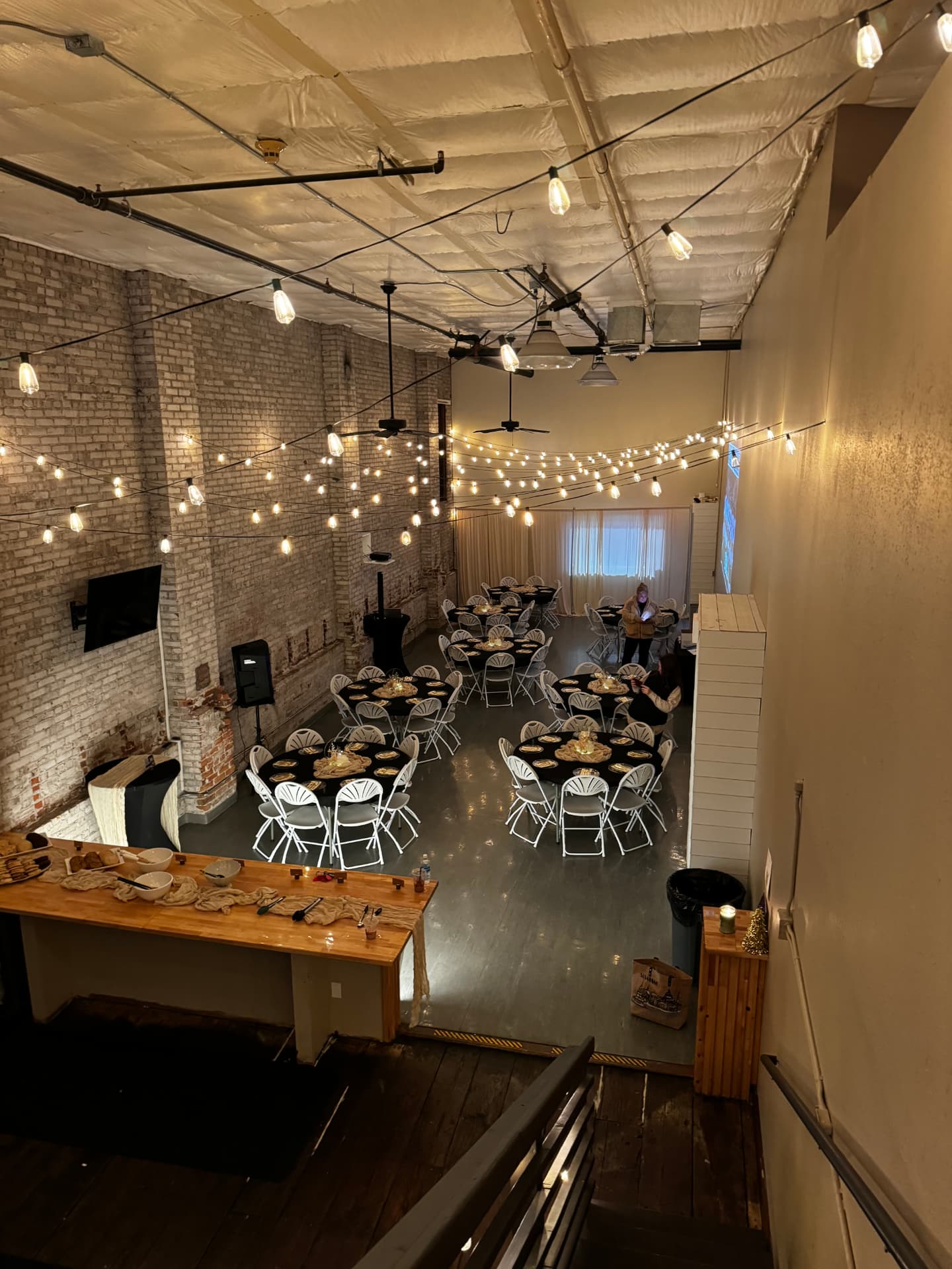 Overhead view of round tables with black linens and gold place settings under string lights at a company Christmas party at Host Wenatchee