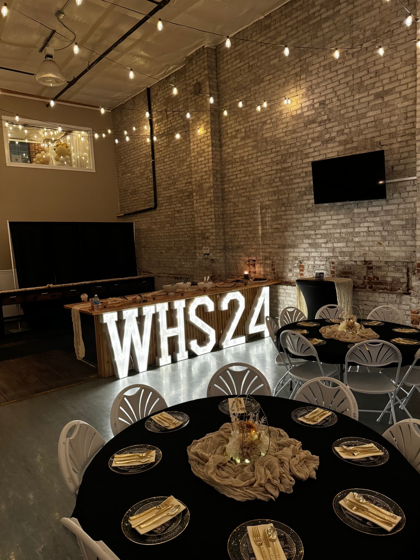 Glowing WHS24 marquee letters, black and gold place settings and round tables at a team banquet celebration at Host Wenatchee