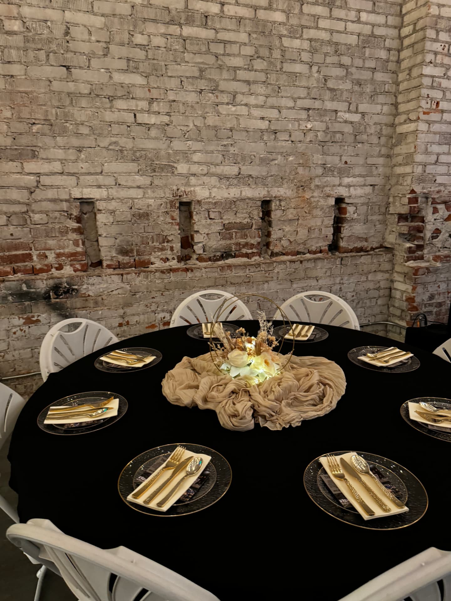 Round table with black linen, gold flatware and a lit floral centerpiece against the brick wall at Host Wenatchee