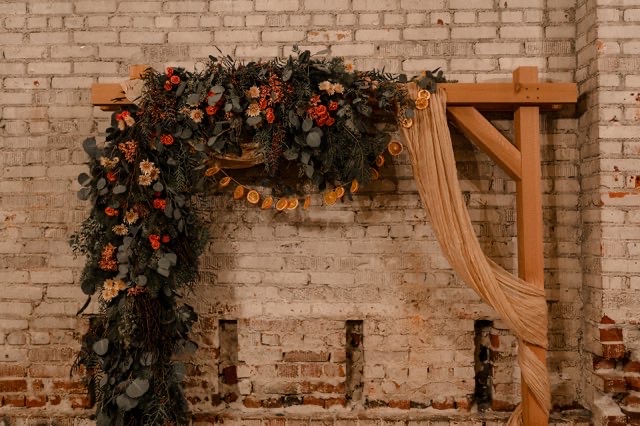 Greenery and dried orange wedding arch against the exposed brick wall at Host Wenatchee