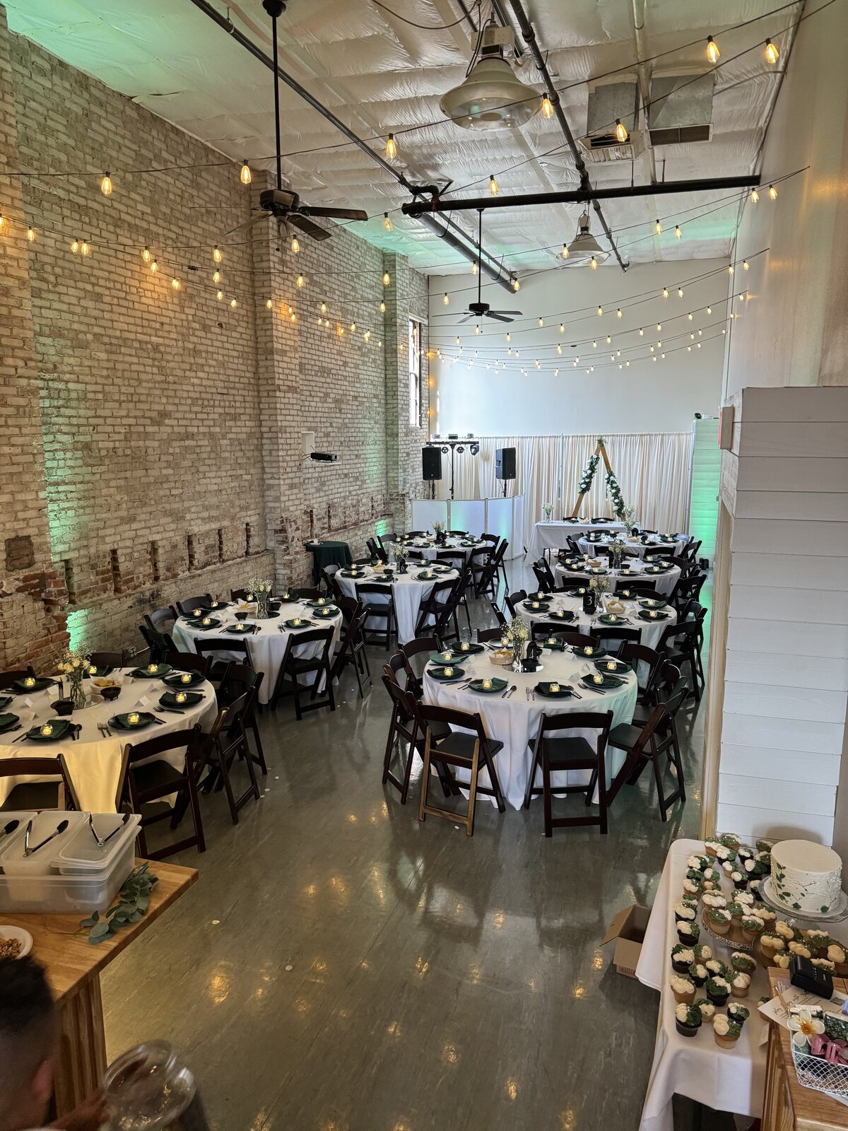 Round tables with white linens, greenery place settings and string lights set for a reception at Host Wenatchee