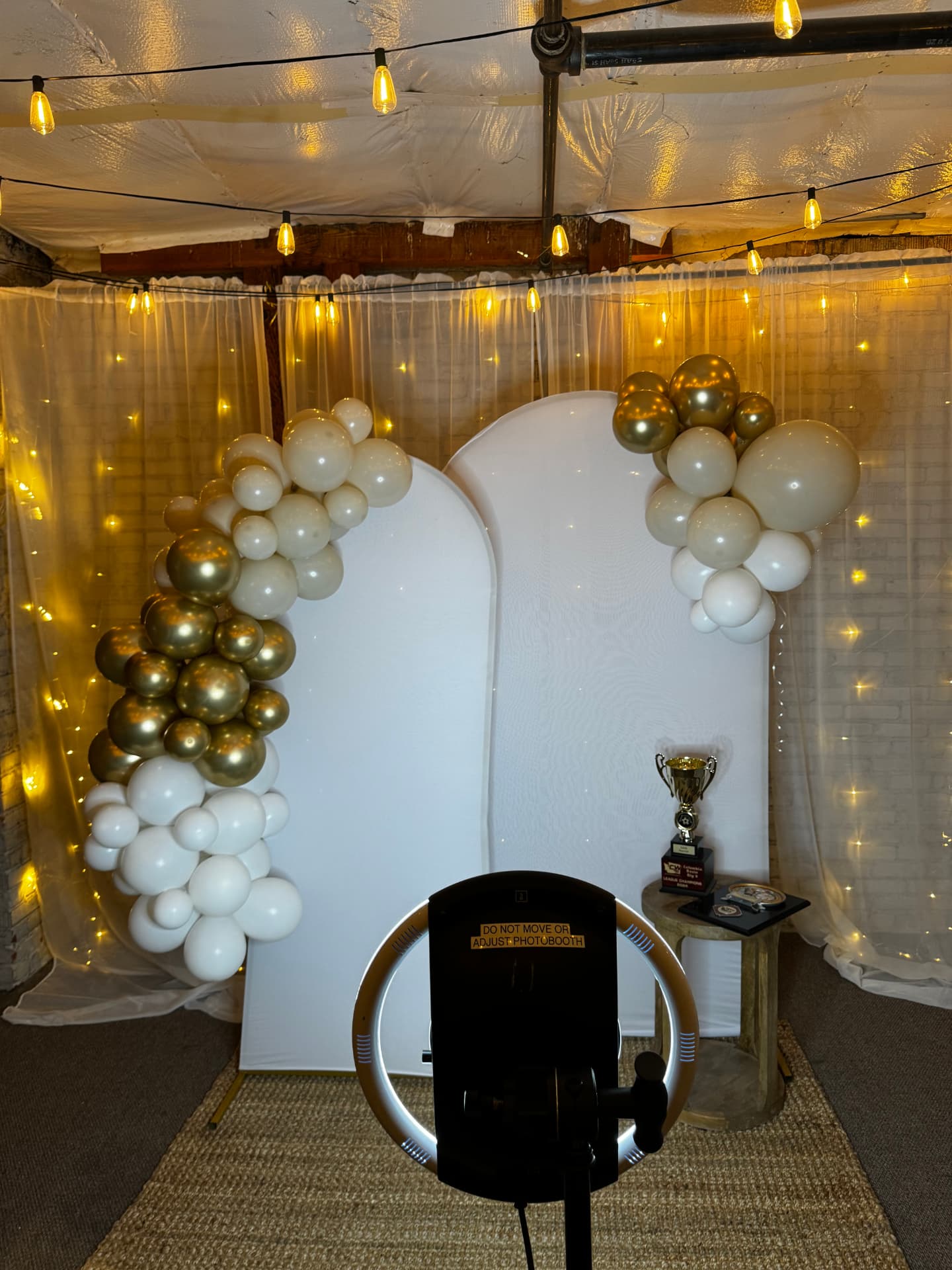 Photo booth with white arch backdrops and a gold and white balloon garland set up at Host Wenatchee
