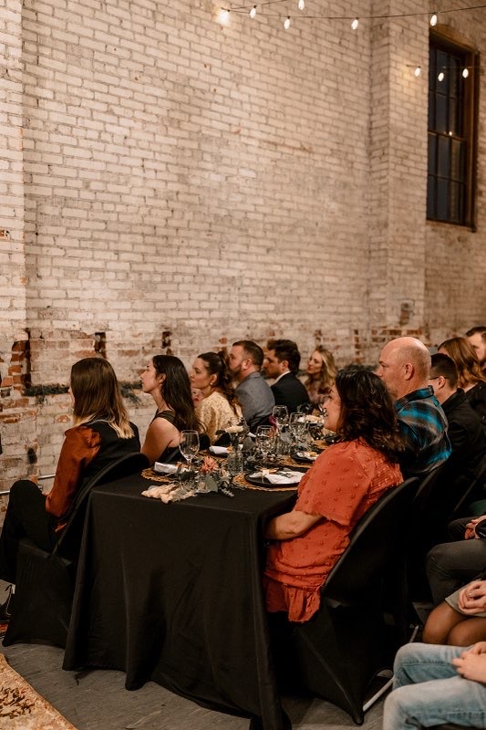 Guests seated at long black-linen tables against the brick wall during a Wenatchee wedding reception