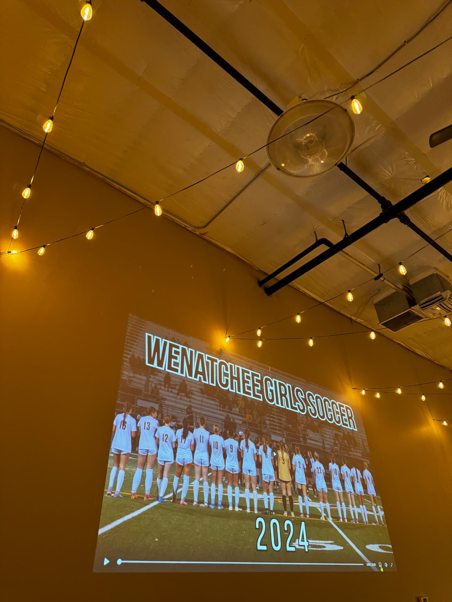 Slideshow projected on the wall under string lights during a celebration at Host Wenatchee