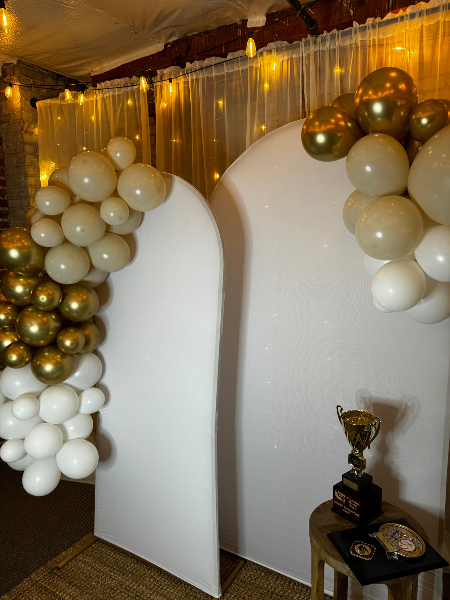 White arch backdrops with gold and ivory balloon garlands and twinkle-light drapery at Host Wenatchee