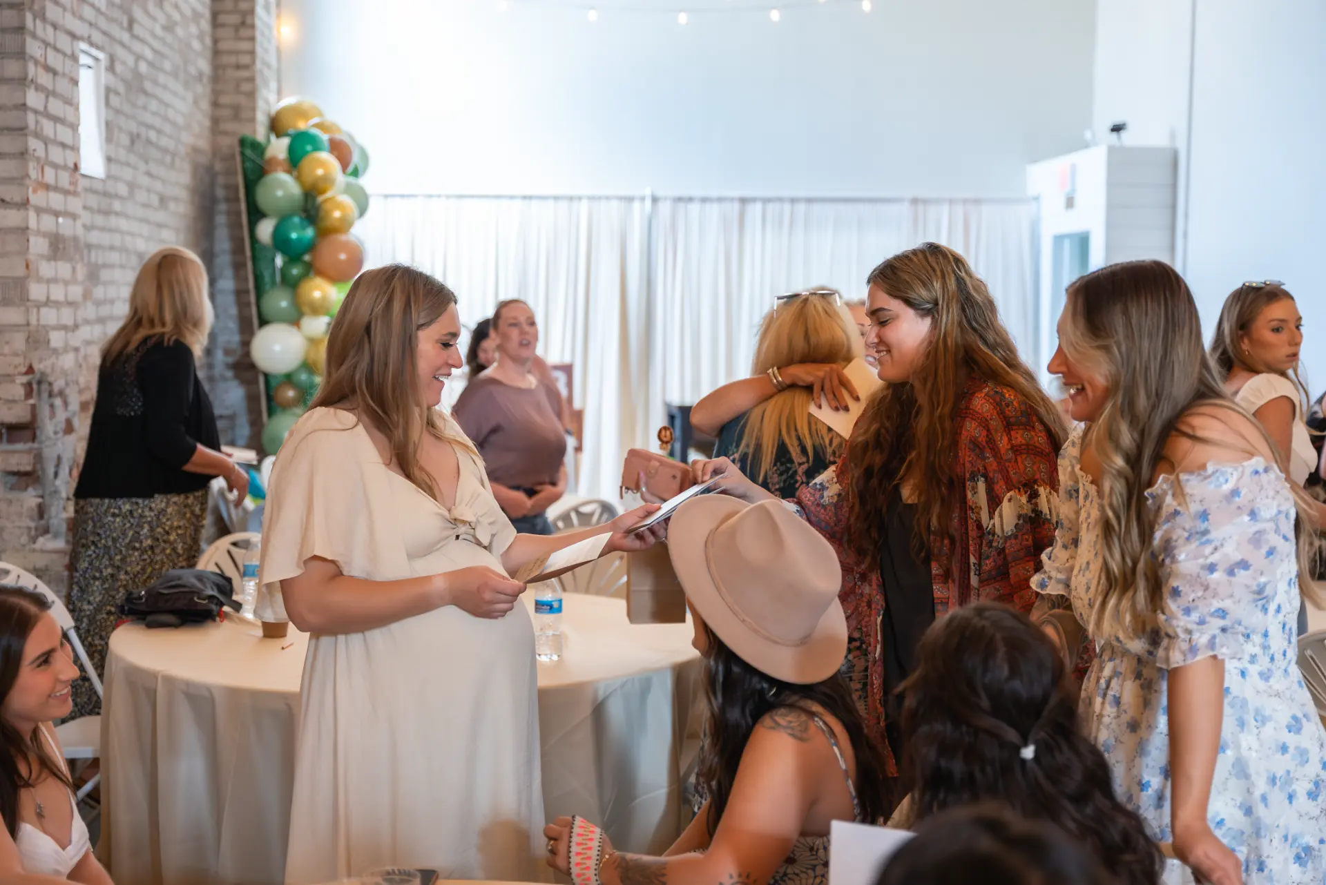 Guests laughing as the mom-to-be opens cards at a baby shower with a green and gold balloon column at Host Wenatchee