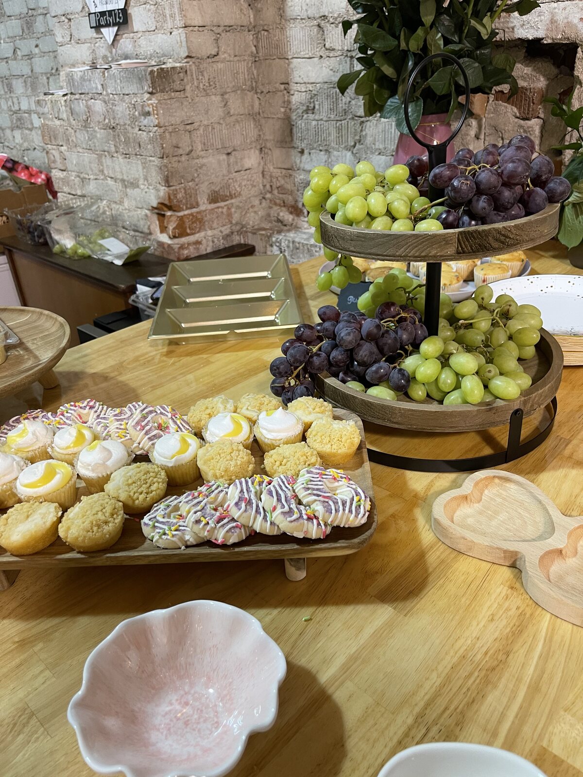 Cookies, mini muffins and a tiered fruit tray on a round table against exposed brick