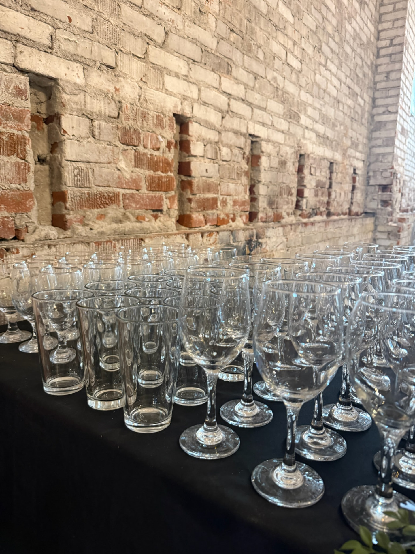 Rows of wine glasses and tumblers on a black-linen table against exposed brick at Host Wenatchee