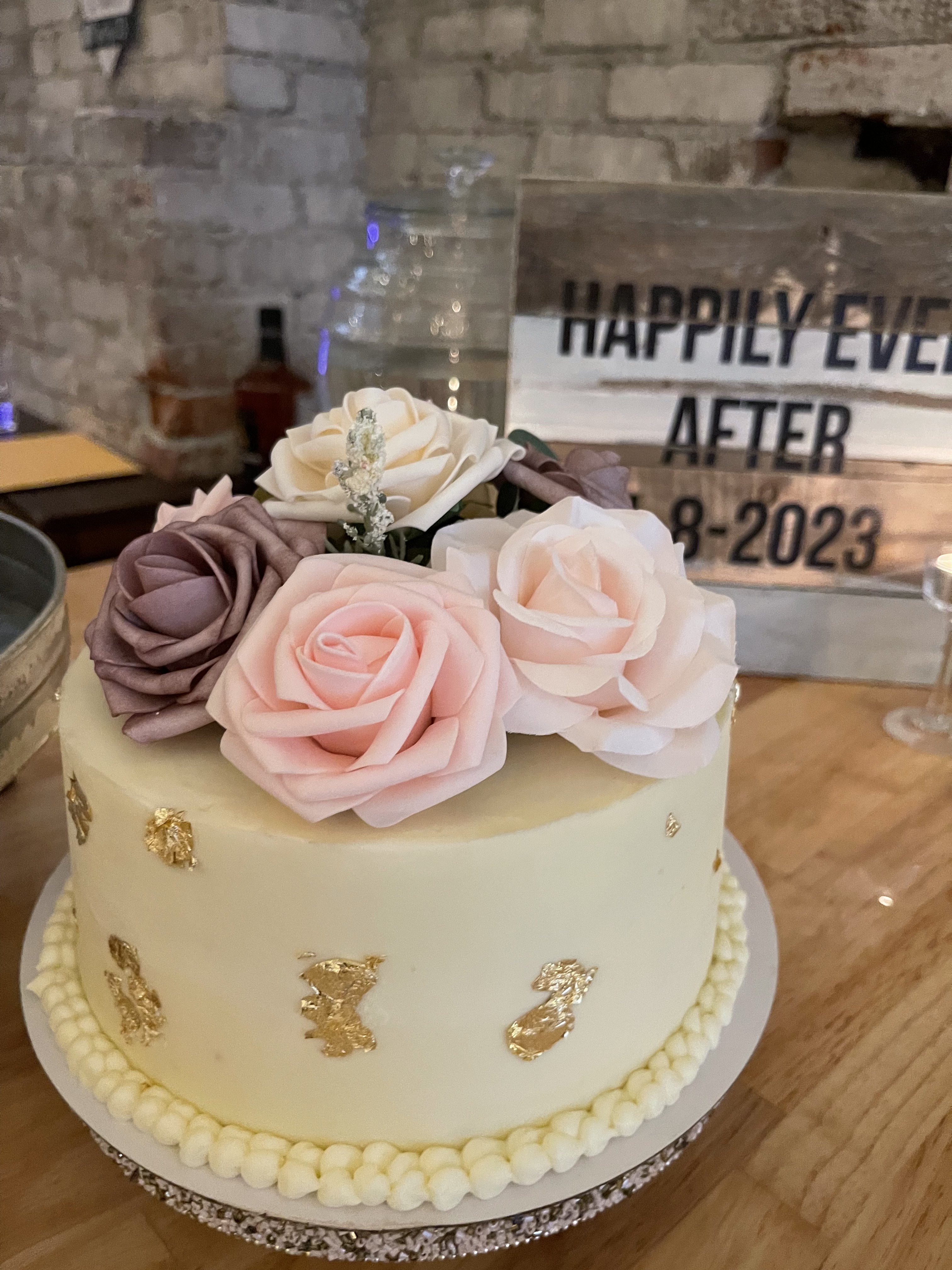 White floral wedding cake with gold leaf beside a Happily Ever After sign at Host Wenatchee